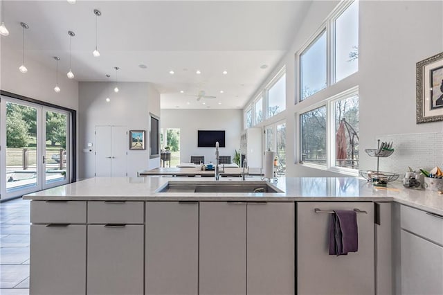 kitchen with light tile flooring, pendant lighting, light stone counters, a high ceiling, and sink