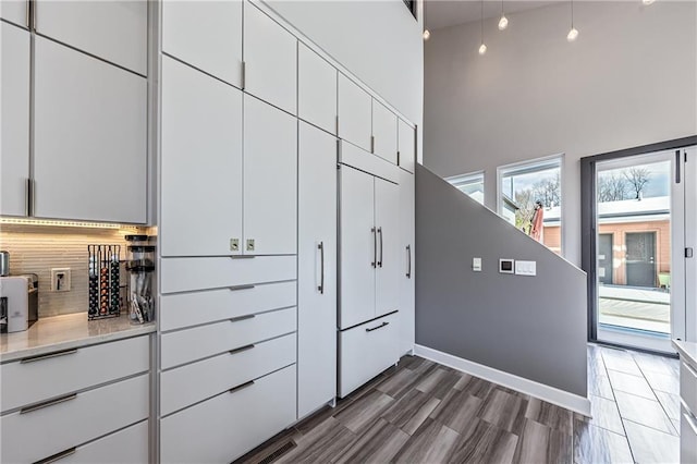 kitchen featuring hardwood / wood-style floors, a towering ceiling, white cabinets, and backsplash