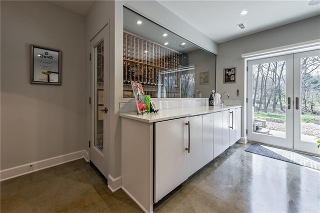 bar with sink, white cabinets, concrete flooring, and french doors