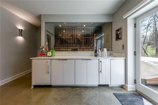 bar with sink, concrete floors, and white cabinetry