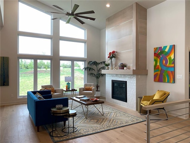 living room featuring high vaulted ceiling, hardwood / wood-style floors, ceiling fan, and a fireplace