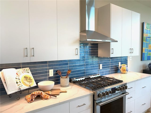 kitchen featuring white cabinetry, stainless steel stove, light stone counters, wall chimney exhaust hood, and backsplash