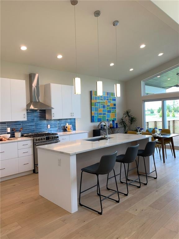 kitchen featuring a center island with sink, light hardwood / wood-style flooring, wall chimney exhaust hood, high end stainless steel range oven, and sink