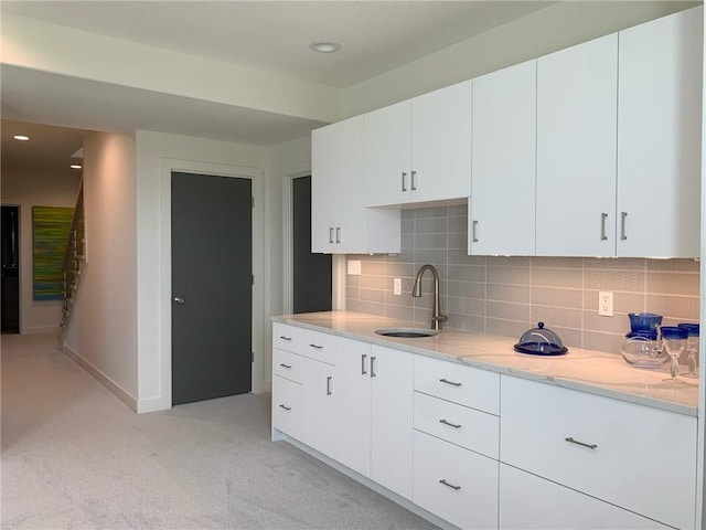 kitchen featuring backsplash, sink, white cabinetry, and light stone counters