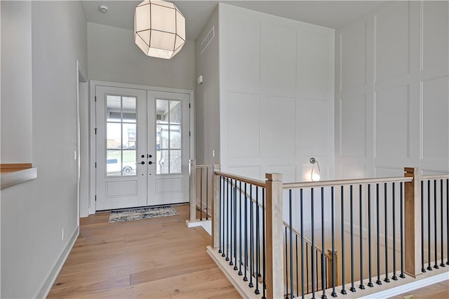 entryway featuring a decorative wall, light wood-style flooring, visible vents, and french doors