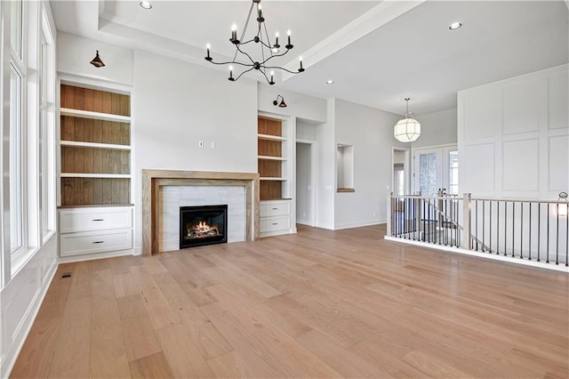 unfurnished living room featuring an inviting chandelier, recessed lighting, a tiled fireplace, light wood-style flooring, and built in shelves