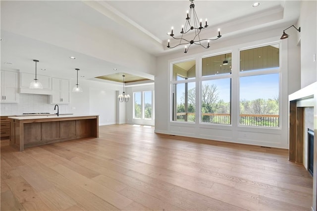 unfurnished living room featuring baseboards, a raised ceiling, a chandelier, light wood finished floors, and a premium fireplace
