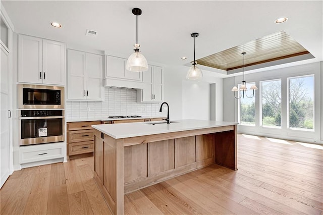 kitchen featuring stainless steel oven, a tray ceiling, gas cooktop, a sink, and built in microwave