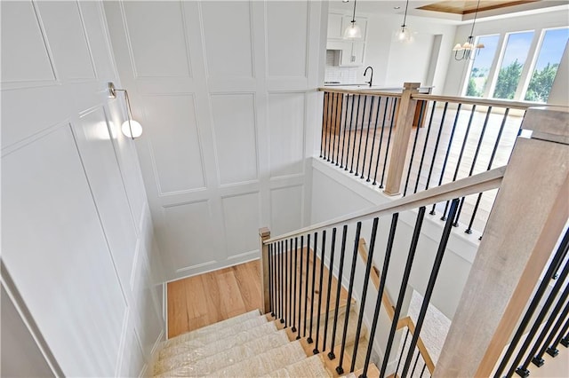 stairs with a decorative wall, a chandelier, and wood finished floors