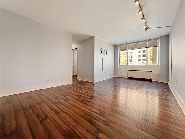 empty room featuring rail lighting, dark hardwood / wood-style floors, and radiator heating unit