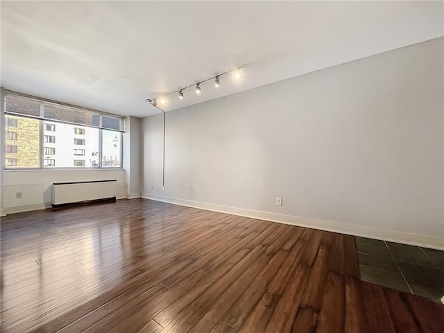 empty room featuring track lighting, dark wood-type flooring, and radiator