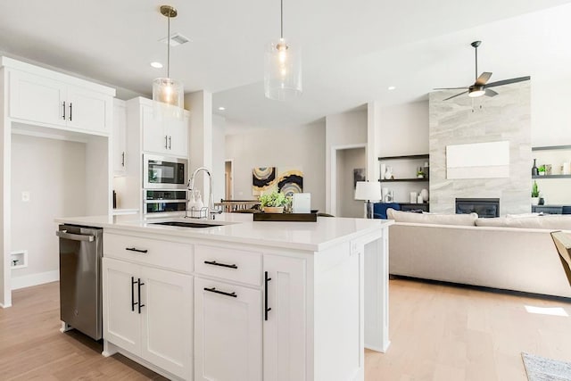 kitchen with pendant lighting, sink, appliances with stainless steel finishes, a kitchen island with sink, and white cabinets