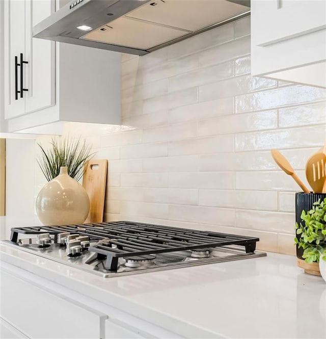 kitchen featuring tasteful backsplash, white cabinetry, range hood, and stainless steel gas cooktop