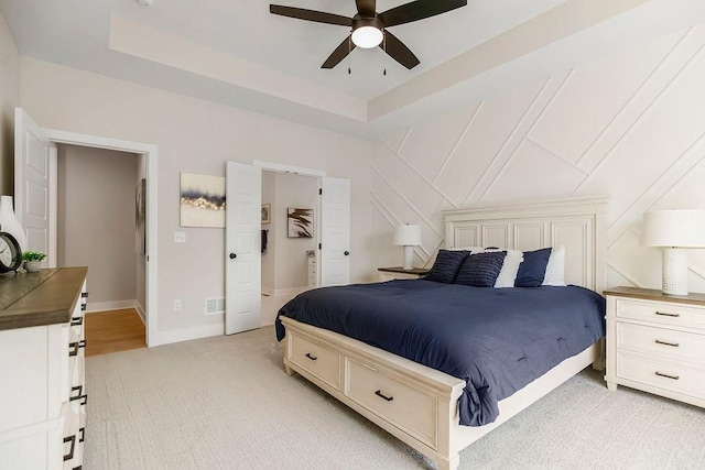 bedroom with light colored carpet, ceiling fan, and a tray ceiling