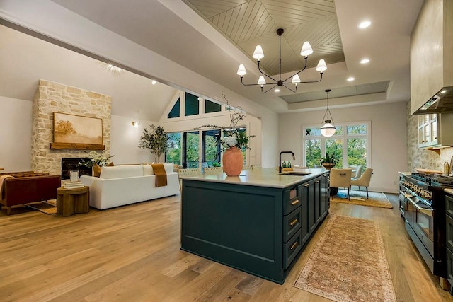 kitchen with light wood-type flooring, sink, a stone fireplace, range with two ovens, and a center island with sink