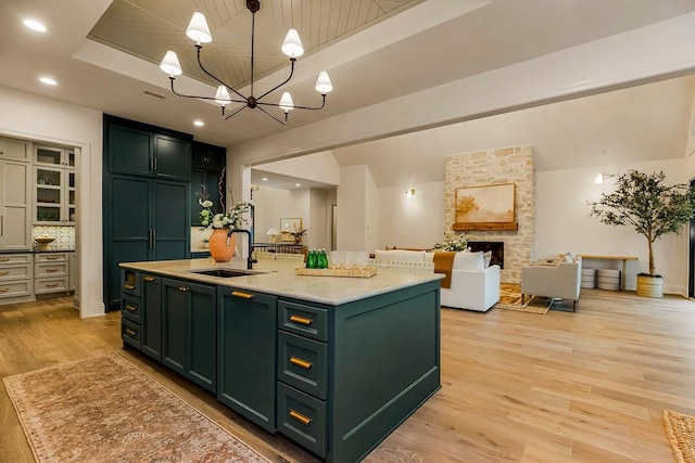 kitchen featuring a fireplace, a center island with sink, light hardwood / wood-style floors, sink, and a chandelier