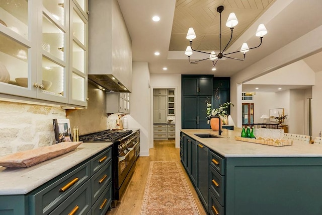 kitchen with hanging light fixtures, light wood-type flooring, sink, premium range hood, and range with two ovens