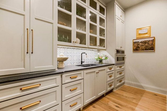 bar with sink, stainless steel oven, tasteful backsplash, and light hardwood / wood-style floors