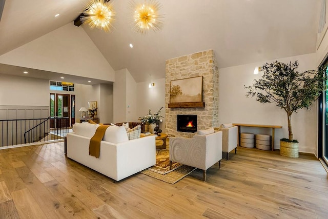 living room with hardwood / wood-style floors, high vaulted ceiling, an inviting chandelier, and a stone fireplace