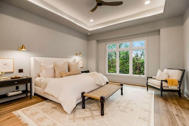 bedroom with light hardwood / wood-style flooring, ceiling fan, and a raised ceiling