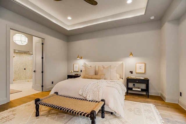 bedroom featuring light wood-type flooring, ceiling fan, a raised ceiling, and ensuite bathroom