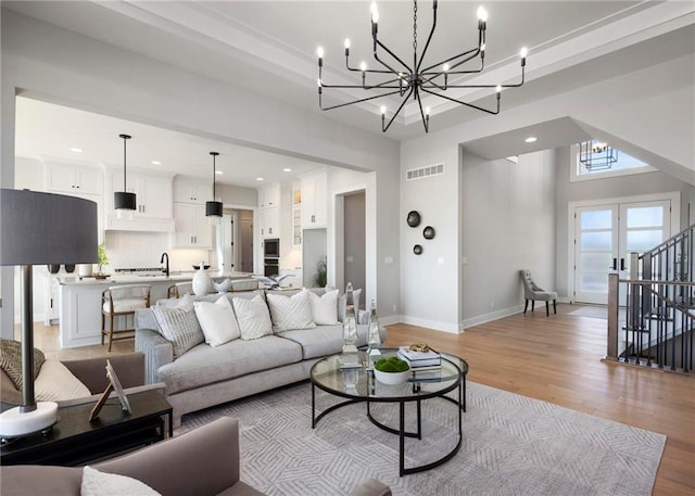 living room with a notable chandelier, light hardwood / wood-style floors, french doors, and sink