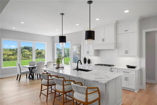 kitchen with a kitchen island with sink, pendant lighting, light stone counters, light hardwood / wood-style floors, and white cabinetry