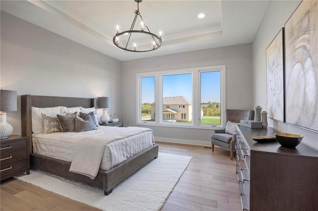 bedroom featuring a tray ceiling, a notable chandelier, and light wood-type flooring