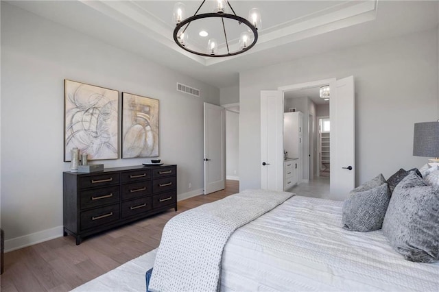 bedroom with an inviting chandelier, light hardwood / wood-style flooring, and a raised ceiling