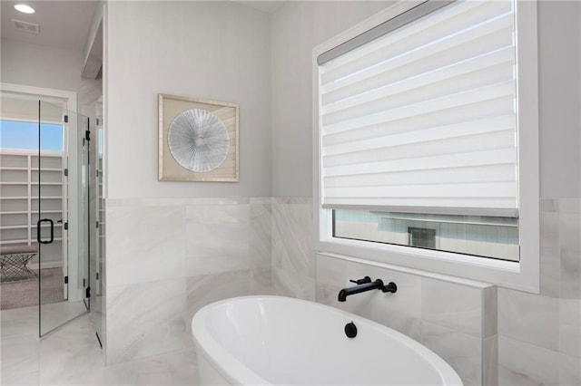 bathroom with tile walls, tile flooring, a healthy amount of sunlight, and a tub