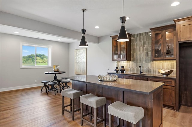 bar with decorative light fixtures, backsplash, sink, and light hardwood / wood-style flooring