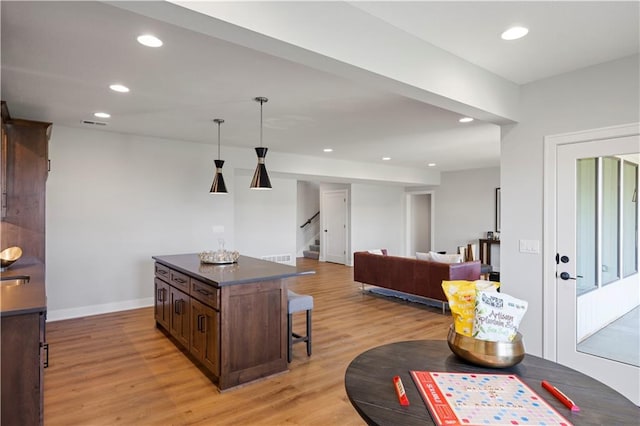 kitchen with hanging light fixtures, light hardwood / wood-style floors, dark brown cabinets, and a breakfast bar