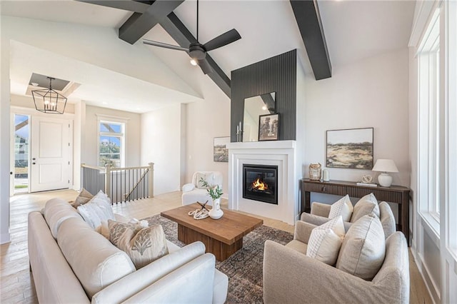 living room with vaulted ceiling with beams, ceiling fan with notable chandelier, and light wood-type flooring