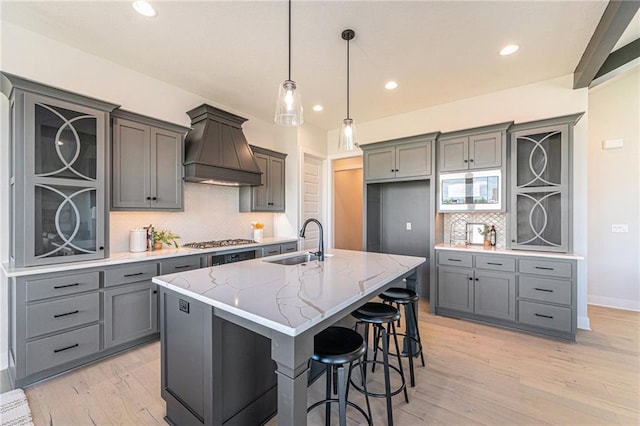 kitchen featuring tasteful backsplash, custom range hood, sink, and a center island with sink