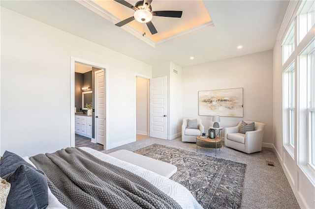 carpeted bedroom with a tray ceiling, connected bathroom, and ceiling fan