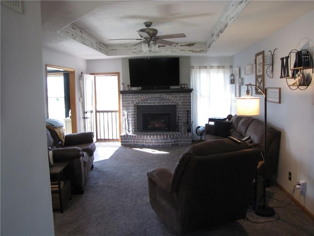 living room with ceiling fan, carpet floors, a fireplace, a raised ceiling, and a textured ceiling