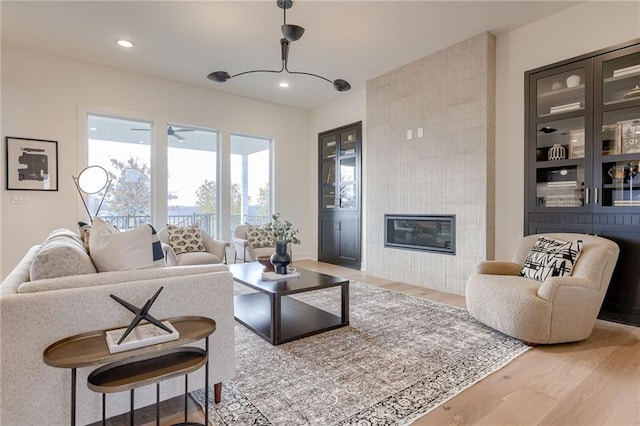 living room with a tiled fireplace, a notable chandelier, and light wood-type flooring