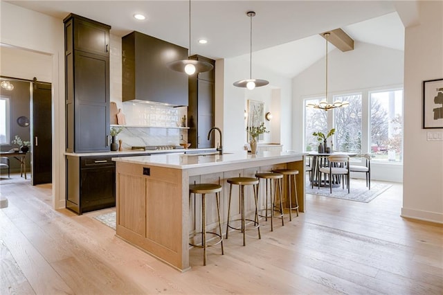 kitchen featuring hanging light fixtures, a center island with sink, a barn door, tasteful backsplash, and light wood-type flooring