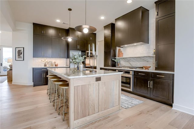 kitchen featuring decorative light fixtures, a breakfast bar, tasteful backsplash, appliances with stainless steel finishes, and light wood-type flooring