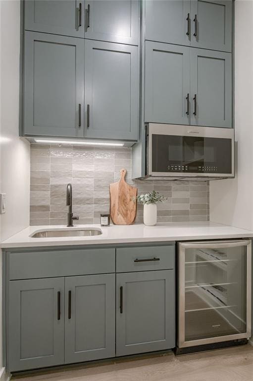 kitchen with backsplash, gray cabinetry, wine cooler, sink, and light hardwood / wood-style flooring