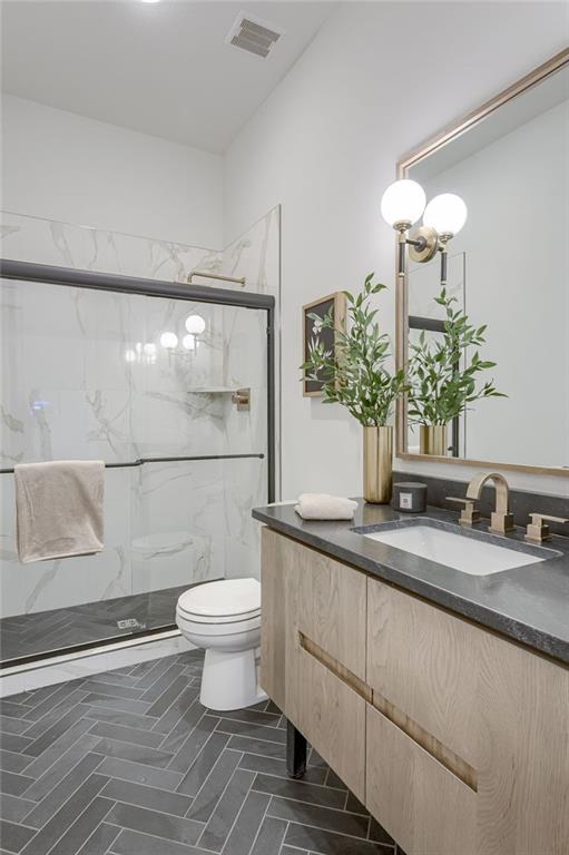 bathroom with tile floors, a shower with shower door, toilet, a chandelier, and vanity with extensive cabinet space