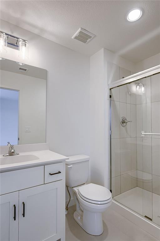 bathroom featuring toilet, a shower with door, a textured ceiling, vanity, and tile floors