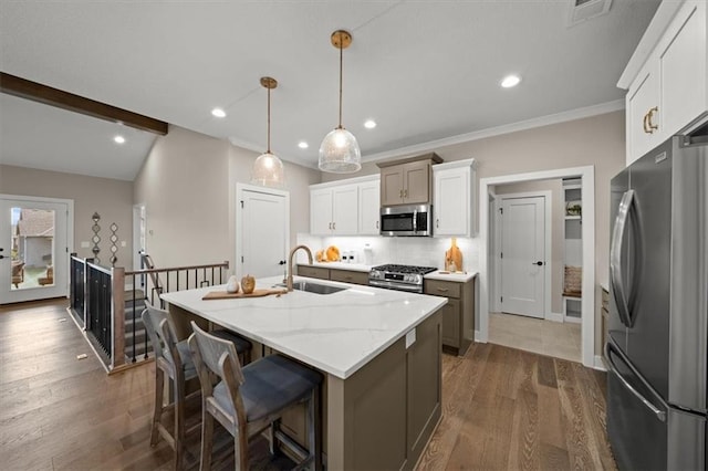 kitchen with white cabinetry, sink, stainless steel appliances, pendant lighting, and a center island with sink