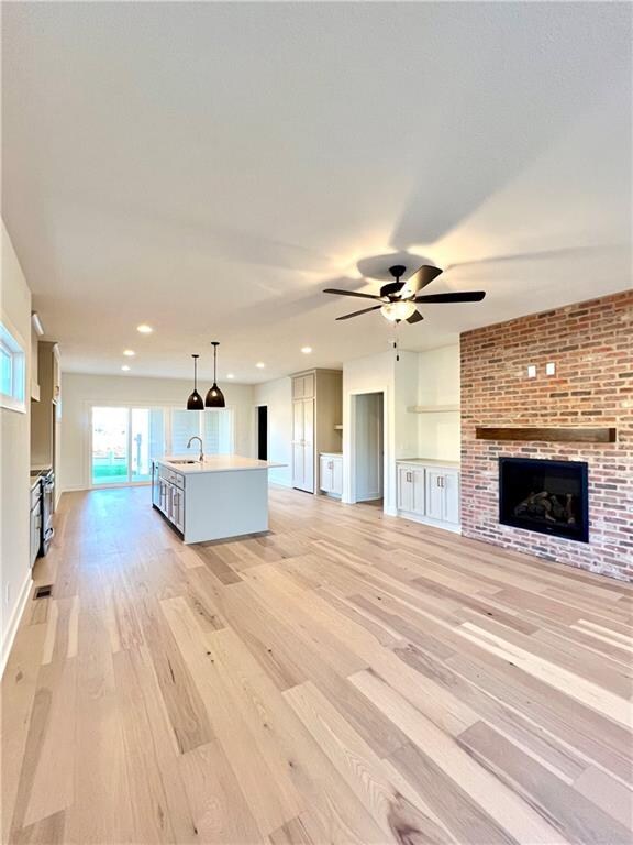 unfurnished living room with sink, a brick fireplace, light wood-type flooring, and ceiling fan