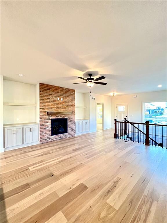 unfurnished living room with ceiling fan, a brick fireplace, and light wood-type flooring