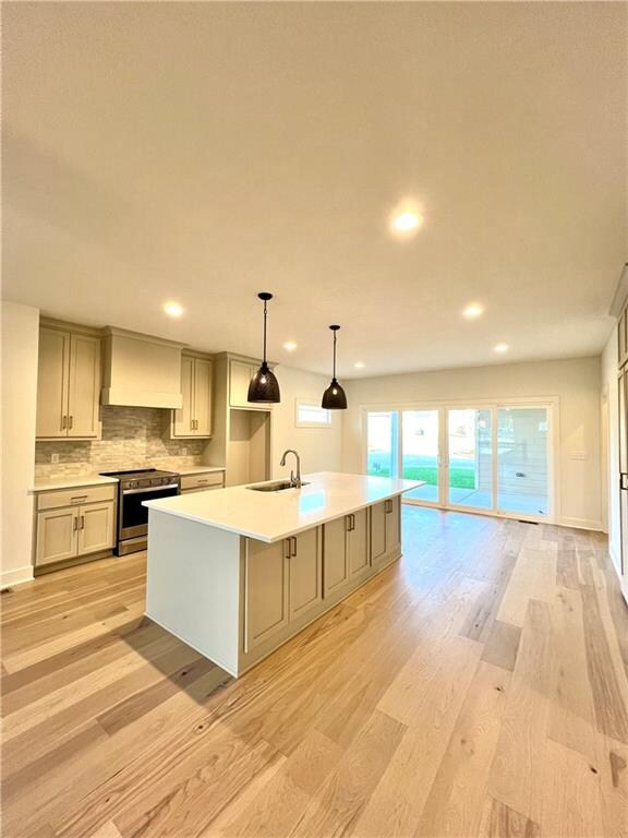 kitchen with sink, stainless steel electric range oven, light hardwood / wood-style flooring, premium range hood, and a center island with sink