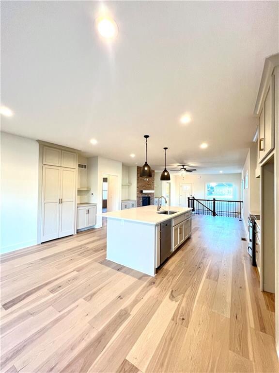 kitchen with hanging light fixtures, an island with sink, dishwasher, gray cabinetry, and light hardwood / wood-style floors