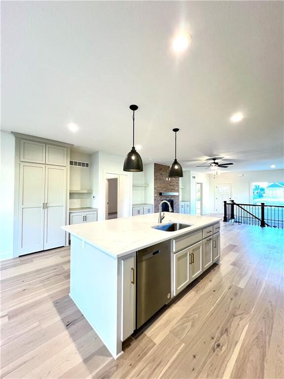 kitchen with an island with sink, light wood-type flooring, dishwasher, pendant lighting, and sink