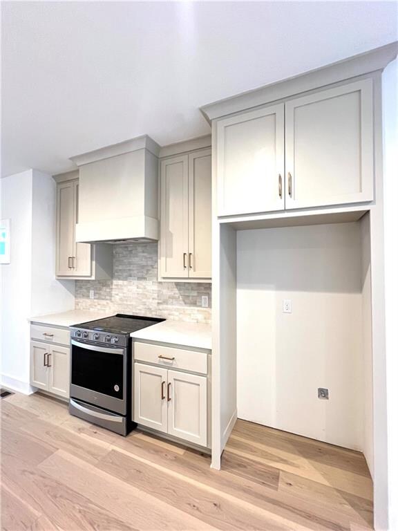 kitchen with light hardwood / wood-style floors, tasteful backsplash, stainless steel range, and custom exhaust hood