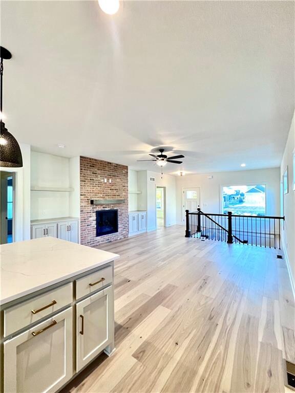 unfurnished living room with a fireplace, light wood-type flooring, and ceiling fan